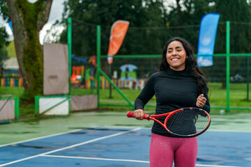 Smiling woman holding tennis racket on court feeling happy
