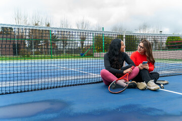 Female friends relaxing on tennis court sharing phone