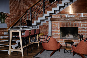 Fototapeta premium Modern business office interior showing empty workspace with computer on desk, high chairs lined up along table, brick walls, staircase, fireplace, cozy seating area, no people visible