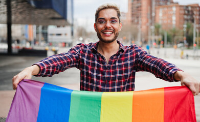 Young gay man with makeup on having fun holding lgbt rainbow flag outdoor - Equal rights for homosexual people and lgbtq concept - Focus on face