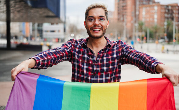 Young gay man with makeup on having fun holding lgbt rainbow flag outdoor - Equal rights for homosexual people and lgbtq concept - Focus on face