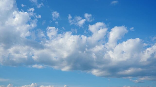 Soft white clouds drift lazily across a clear blue sky on a bright afternoon. The peaceful atmosphere enhances the beauty of the countryside. Nature displays its calm charm. Dramatic sky