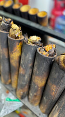lemang bambu, made from glutinous rice wrapped in banana leaves and cooked inside charred bamboo tubes, slowly roasts over fire. The golden tops show the traditional method of preparing this dish