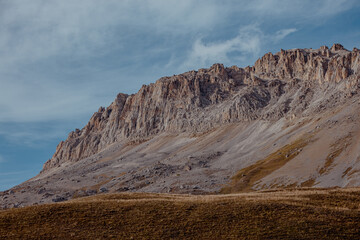 Rugged mountain landscape with rocky cliffs and a clear blue sky. The terrain is dry with sparse vegetation, showcasing natural geological formations.