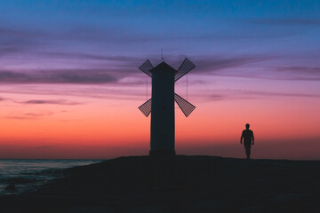 One man silhouette walk along the pier near the lighthouse on the sea at sunset