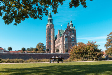 Three elderly people sitting on a bench opposite Rosenborg Castle, the concept of recreation of old people in a big historical city