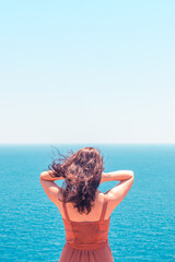 Young brunette girl in red dress looking at turquoise seascape and enjoying summer vacation