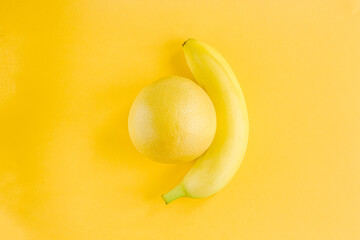 Yellow glowing banana and orange lie on a yellow background, the concept of creativity and fruit design