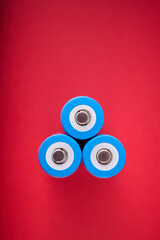 Three blue rechargeable lithium batteries, size 18650, on a red table.