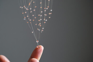 Arrangement of Small Bead Strings Held by Finger Displaying Gravity and Suspension with Gray Background Elegant Craft Delicate Art