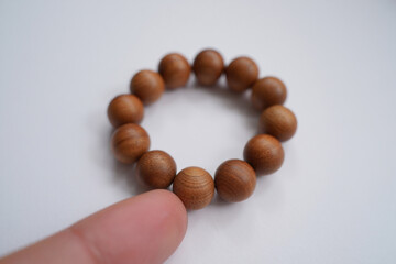 Beaded Wooden Bracelet Held By Finger Displaying Natural Round Shape Smooth Texture and Detail on White Tabletop Simple and Clean
