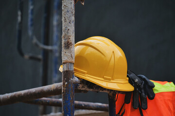 Safety on Site: A close-up showcases a bright yellow safety helmet resting on weathered scaffolding, accompanied by protective gloves and a high-visibility vest.