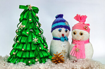 A couple of snowmen sitting next to a christmas tree in the snow
