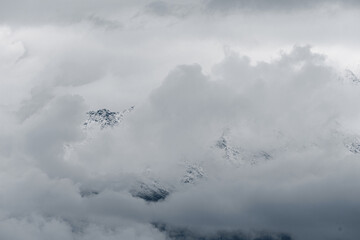 Snow-capped mountains rise above a dark, forested landscape under a cloudy sky. The scene captures the beauty of nature in a dramatic setting.
