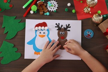 Little boy making Christmas postcard at wooden table, top view. Child handmade craft