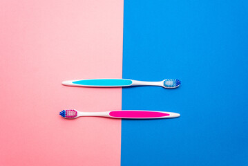Two vibrant toothbrushes are placed side by side on a split background of pink and blue. The striking colors enhance the visual appeal of daily dental care essentials