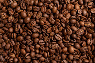 A close-up, high-resolution image of roasted coffee beans. The frame is completely filled with whole, glossy Arabica beans in warm brown tones, showing rich texture, natural cracks