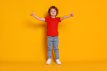 Cute little boy showing thumbs up on orange background