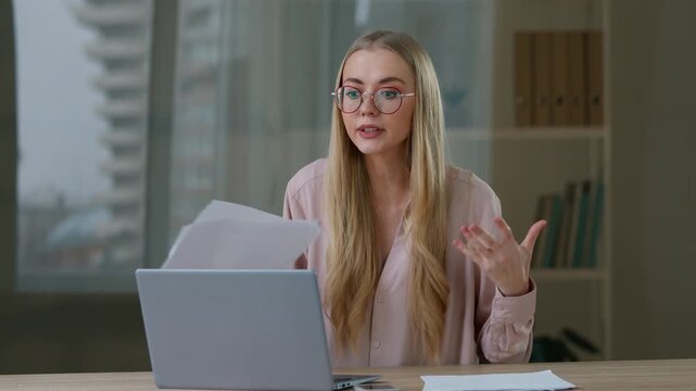 Angry Caucasian business woman talking video call with papers laptop in office stressed businesswoman female leader girl negative conversation conference quarrel discuss documents mistake break report