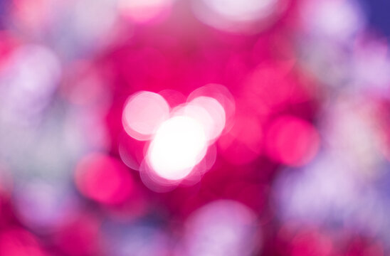 Defocused photography features bokeh effect dominated by pink and magenta colors. Blurred circles of light overlap, with cluster of bright white circles centered in the frame. Abstract background.