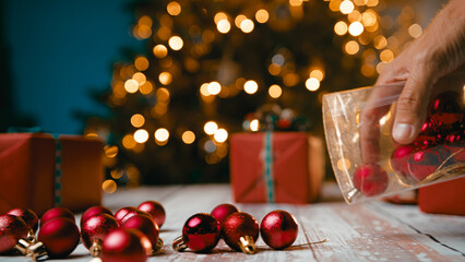 Small red Christmas ball decorations fall on a table in front of the tree