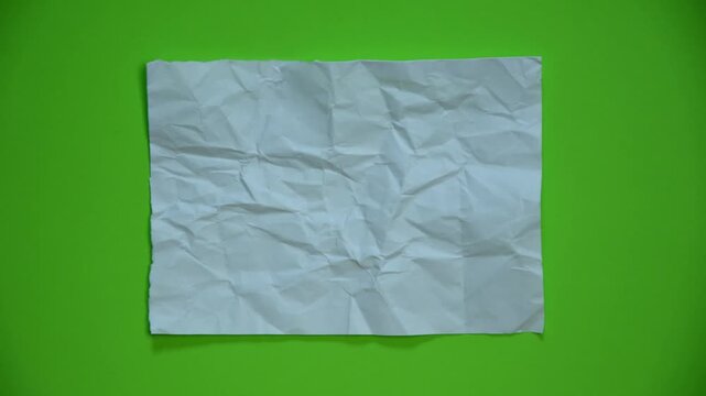 Crumpled and wrinkled piece of white paper, partially unfolded from a ball, isolated on a green screen