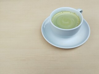 Matcha latte hot drink in white cup with wooden table background. High angle view. Copy space 