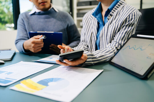 Business documents on office table with smart phone and calculator digital tablet and graph business with social network diagram and two colleagues discussing data working in the office
