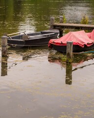 Fototapeta premium Two boats moored at wooden pier on calm lake covered with duckweed