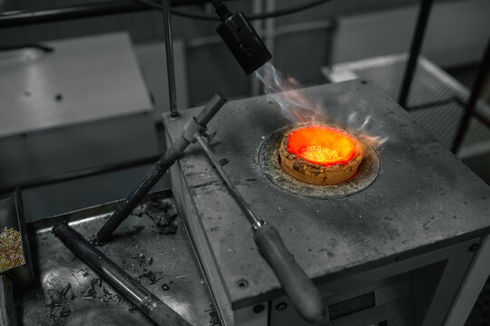 Molten metal glows within a crucible as it's heated by a torch during a jewelry-making process.