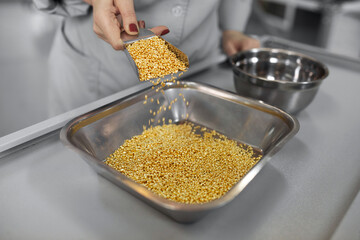 Golden grains pour into a metal container, suggesting fresh ingredients and culinary preparation.