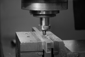 A close-up shows a metal cutting tool precisely carving into a rectangular block of material on a milling machine.