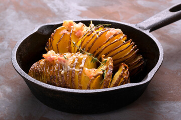 Hasselback potato roasted with cheese, bacon and aromatic herbs served in cast iron skillet on a...