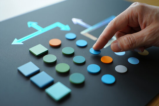 Finger Selecting Blue Circle from Colorful Geometric Shapes on Dark Surface Indicating Choice and Decision Making Process
