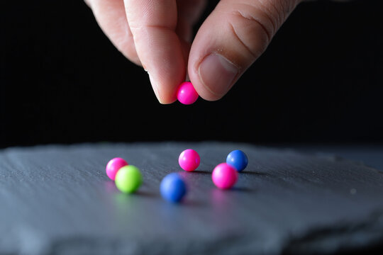 Hand Picking Pink Spheres from Colorful Set on Dark Background for Creative Play Abstract Design Concept Close up