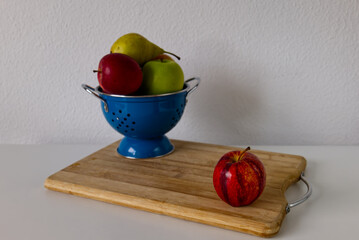 Fresh apples and pears in a blue colander on a wooden board in the kitchen. Colorful assortment of fresh fruits. Healthy eating, cooking, local and sustainable consuming, and grocery concepts.