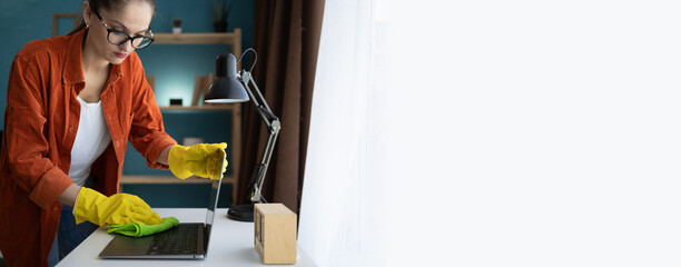 Housewife in rubber yellow gloves cleaning laptop in home office. copy space