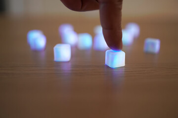 Finger Pressing on Glowing Blue Cube with Blur Light Background on Wooden Table Surface for Creative Technology Concept 150 Characters