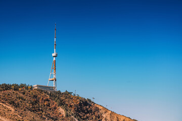 Tbilisi, Georgia cityscape showing the prominent Mtatsminda TV tower standing tall on a mountain with a clear blue sky