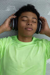 Close up of a teenage athlete lying on an exercise mat with his eyes closed, listening to music and holding his headphones. A moment of relaxation after working out