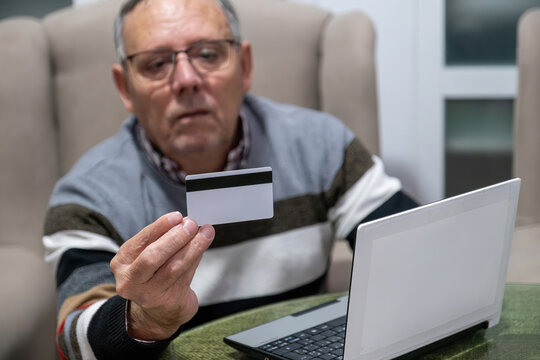 Senior man performing online shopping with credit card and laptop