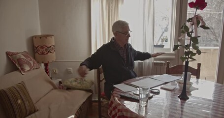 An active senior man performs gentle stretching exercises and arm movements at his home table, maintaining his health and fitness. - Powered by Adobe