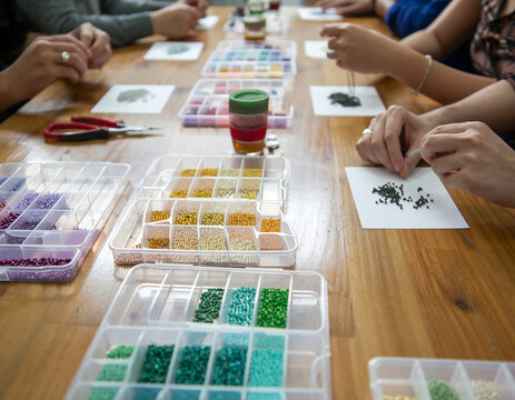 Close-up of hands working on bead art or jewelry making workshop with colorful seed beads on wooden table