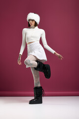 Young woman showcasing chic winter fashion against a vibrant pink backdrop in a stylish pose
