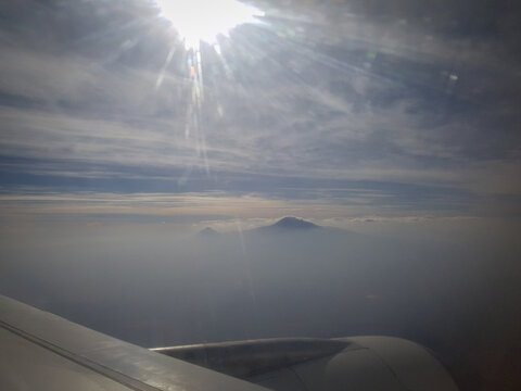 Flying over the sky, a mountain emerges from the dust of the earth. View from the airplane window during flight - Powered by Adobe