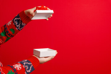 Hands opening a white gift box with red bow on a clean red background, perfect for holiday visuals,...