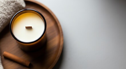 Scented candle on wooden plate with cinnamon stick and towel  