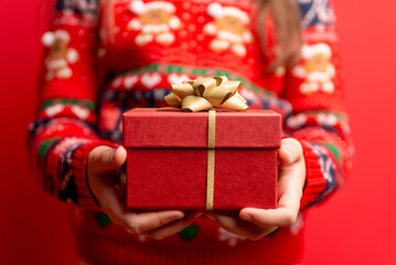 Child presenting a red gift box with a gold bow on a bold red background, suitable for holiday cards, promotions, and festive campaigns