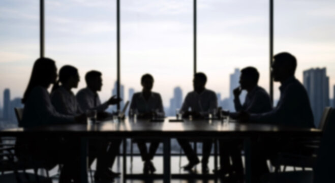Blurred silhouettes of diverse professionals around a modern conference table in a sleek glass-walled office, suggesting collaboration.