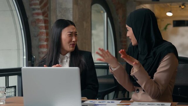 Two multiethnic business women team in office looking computer shocked emotion negative amazed Asian woman Muslim Islamic girl diversity females businesswomen watching disgusting video closing eyes